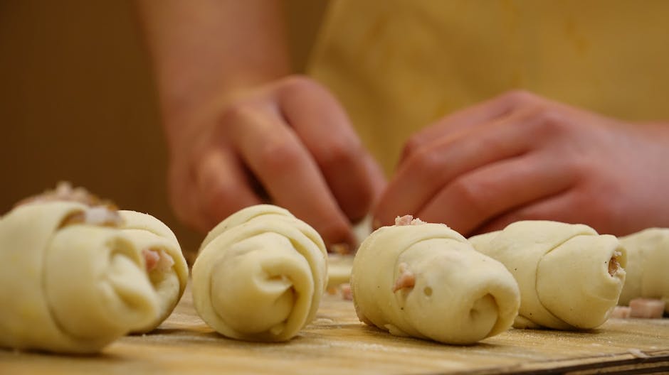 Hands expertly rolling dough in a bakery kitchen, ready for baking.