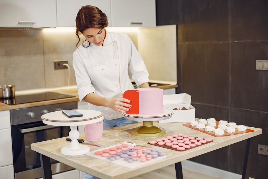 Concentrated skilled woman in uniform smoothing outer layer of cake with scraper during production of desserts and pastries in confectionery