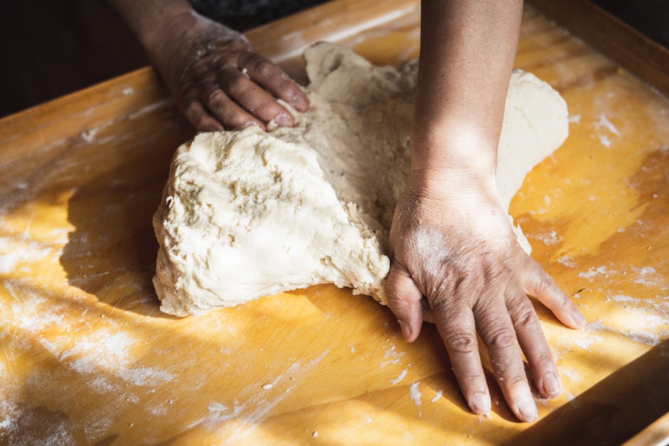 A person kneading dough on a floured wooden surface, bathed in natural light.
