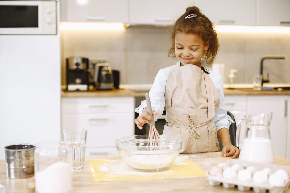 Young girl smiling while baking in a kitchen, mixing ingredients in a bowl.