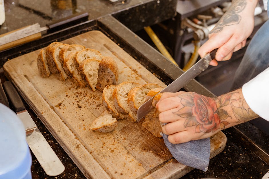 A tattooed chef slicing fresh artisan bread on a wooden board in a kitchen setting.