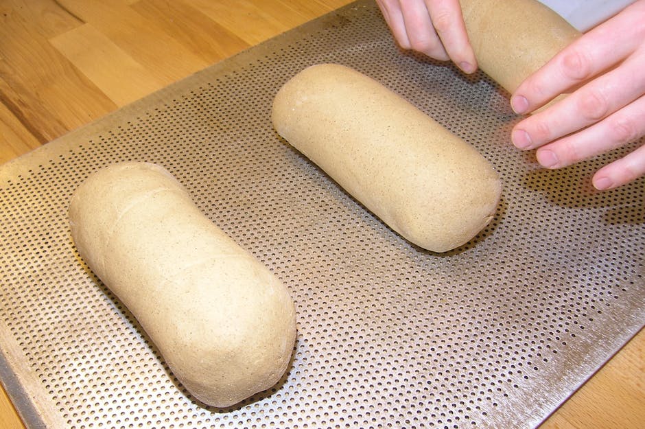 Close-up of hands preparing homemade bread dough on a baking tray, emphasizing traditional baking methods.